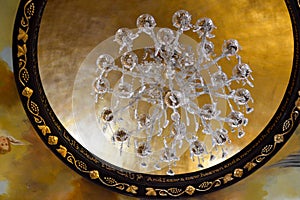 Large beautiful luxurious crystal glass chandelier with pendants and patterns and a frame of gold ornaments on a high stone ceilin