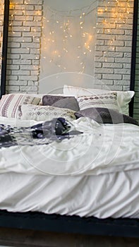Large bed with pillows and blankets indoors. Glowing garland over bed. Interior design room in studio.