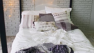 Large bed with pillows and blankets indoors. Glowing garland over bed. Interior design room in studio.