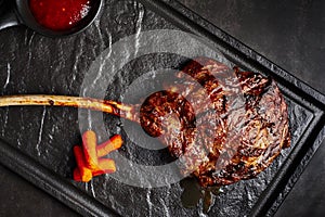 Large beef tomahawk steak with sauce at black stone background garnished with french fries photo