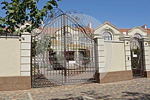 A large black iron gate with a forged pattern of metal rods and a gray concrete fence wall
