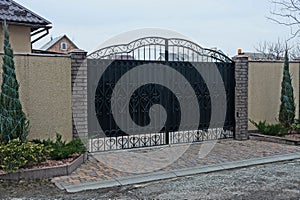 A large black iron gate with a forged pattern and part of a gray concrete fence