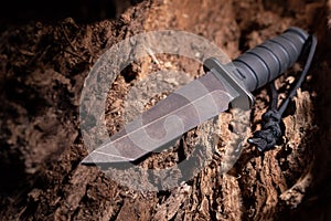 A large black knife in medium logs. A large army knife.