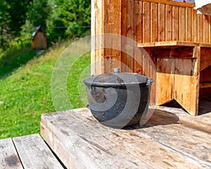 A large, black from soot, the cauldron, the pot stands on the edge of a wooden house.