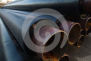 Large black steel pipe with heat insulation on the construction site close up in a plastic tube wrapper