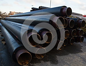 Large black steel pipe with heat insulation on the construction site in a plastic tube wrapper lying
