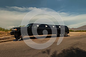 Large black stretch limousine on a tire jack on the side of a road