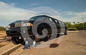 Large black stretch limousine on a tire jack on the side of a road