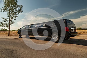 Large black stretch limousine on a tire jack on the side of a road