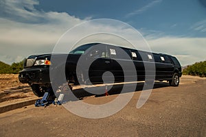 Large black stretch limousine on a tire jack on the side of a road