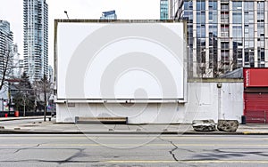 Large, blank billboard stands prominently in an urban environment, surrounded by high-rise buildings and city photo