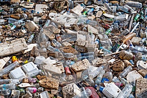 Large blockage pile of garbage stretches parallel to the river - plastic, rubber, and others. Waste petroleum products