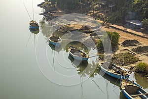 Large blue fishing boats on the shore on the smooth water against the green jungle and huts