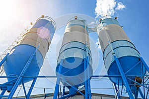 Large blue industrial tanks for cement, sand, water. Blue sky background with white clouds