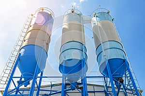 Large blue industrial tanks for cement, sand, water. Blue sky background with white clouds. Bottom view