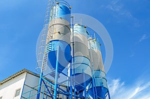 Large blue industrial tanks for cement, sand, water. Metal stairs leading to metal containers. Side view