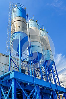 Large blue industrial tanks for cement, sand, water. Metal stairs leading to metal containers. Vertical photo