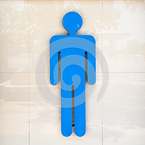 Large blue men\'s toilet sign on a tiled wall. Copy space background