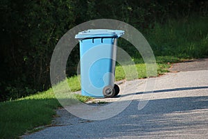 a Large blue plastic trash can for waste paper stands alone on the side of the road, waiting to be picked up