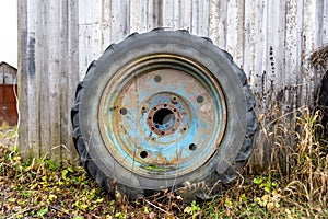 a large blue rusty wheel from a tractor stands near the wall of the barn