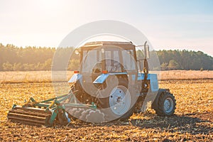 Large blue tractor plow plowed land after harvesting the maize crop on a sunny, clear, autumn day.