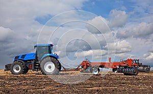 A large blue tractor, plowing field against the beautiful sky.