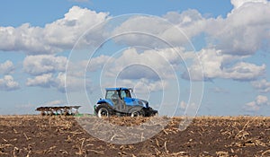 A large blue tractor, plowing field against the beautiful sky