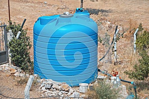 Large blue water tank near a private farm or garden in a dry area. Concept of equipment for agriculture and drought