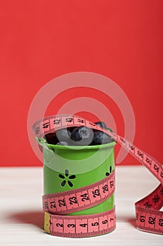 Large blueberries in a decorative bucket. Measuring tape for measuring the waist. International day without diets. Close-up