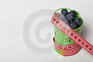 Large blueberries in a decorative bucket. Measuring tape for measuring the waist. International day without diets. Close-up