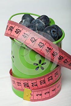 Large blueberries in a decorative bucket. Measuring tape for measuring the waist. International day without diets. Close-up