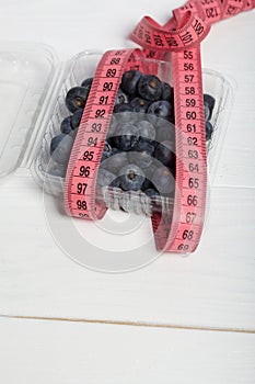 Large blueberries in a decorative bucket. Measuring tape for measuring the waist. International day without diets. Close-up