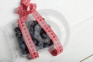 Large blueberries in a decorative bucket. Measuring tape for measuring the waist. International day without diets. Close-up