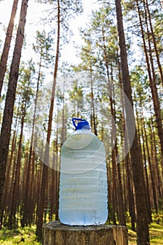 A large bottle of fresh clean drinking water is standing on a stump in the forest