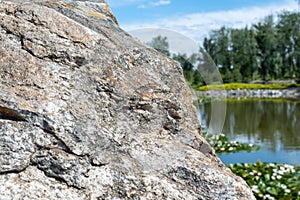 Large boulder in city park. Big stone near artificial decorative pond.
