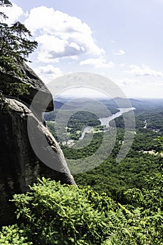 A large boulder frames a scenic view of Chimney Rock Park.