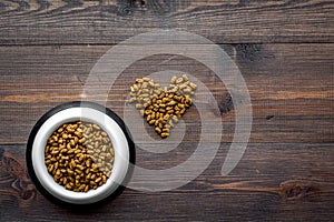 Large bowl of pet - cat food spilling in heart shape on wooden background top view mockup