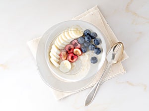 Large bowl of tasty and healthy oatmeal with fruits and berry for Breakfast, morning meal. Top view, white marble table