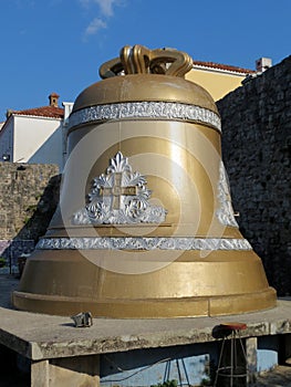 Large bronze bell on a concrete pedestal. Silver ornament and gold cross