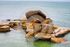 Large brown beige stone pile weathered uneven in the ocean green transparent water background stone beach