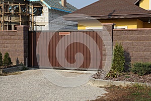 Large brown metal gate and brick fence