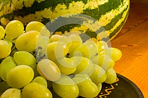 large brush of green grapes and watermelon in a dark ceramic plate on a wooden background