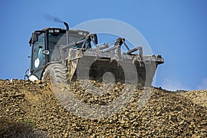 Large bucket with the earth of an escalator frontally on a sunny hot day pours soil against the sky.Global construction. Bottom