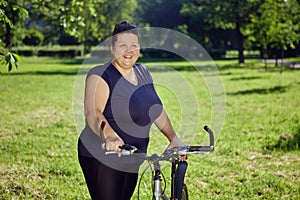 Large Build Caucasian woman rides a bicycle in the park on a sunny summer day.