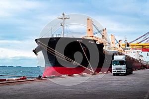 Large bulk cargo ship berthing at port discharging cargo. Truck leaving terminal after loading cargo.