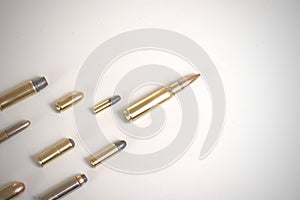 A large bullet 7.62 x 51mm NATO leading a group of several other bullets laying over a white surface.
