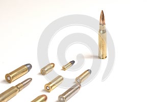A large bullet 7.62 x 51mm NATO standing in front of several other bullets laying over a white surface