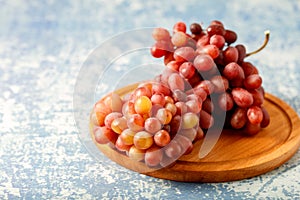 Large bunch fresh pink red grapes on wooden board on blue background