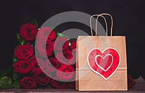 Large bunch of red roses and a gift bag with a heart.