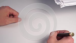 A large bundle of paper falls on a white office desk in front of an employee with a pen in his hand